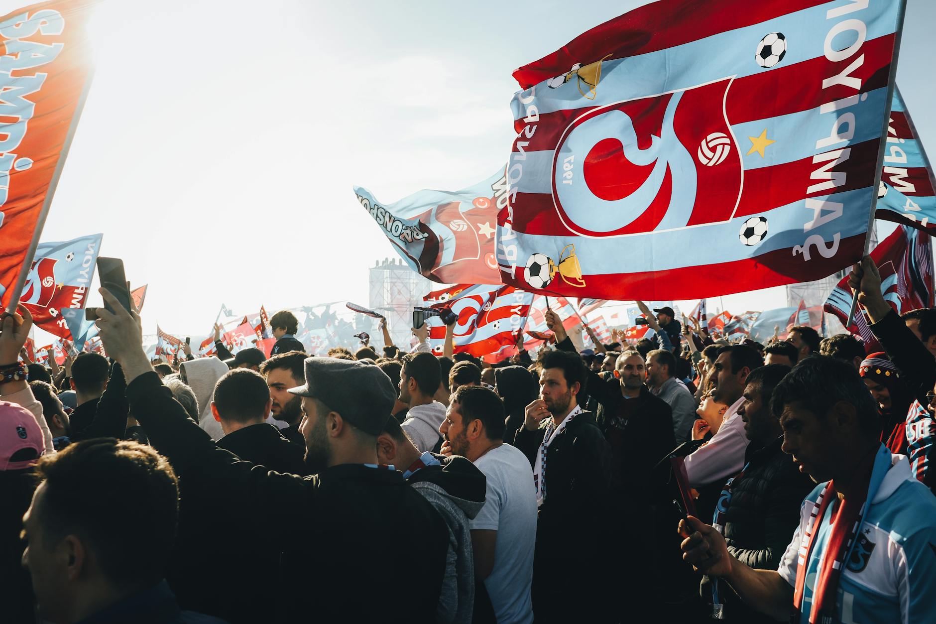 Tłum kibiców machających kolorowymi flagami na słonecznym stadionie