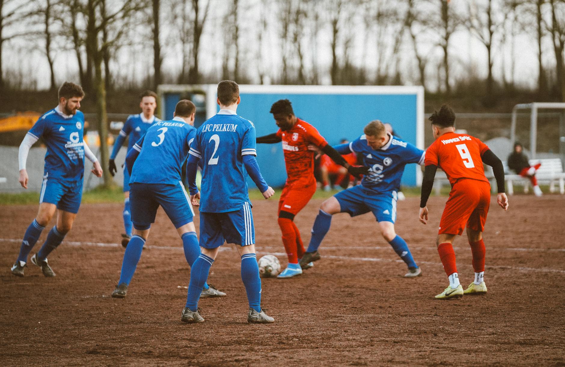 Amatorski mecz piłkarski drużyn w niebieskich i czerwonych strojach na błocie