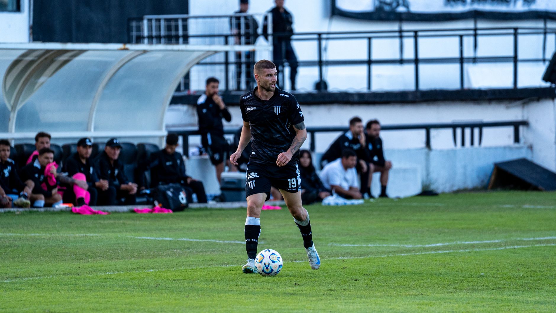 Jak wygrywać mecze w EA FC w 90. minucie: zarządzanie tempem i zmiany z ławki Piłkarz drybluje z piłką, a rezerwowi obserwują mecz zza linii