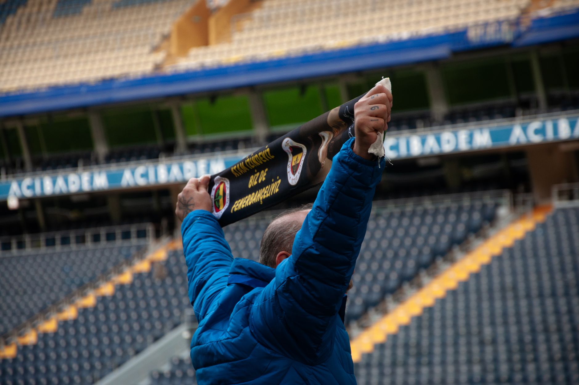 Jak rozpoznaje się oryginalne szaliki i programy meczowe: mini poradnik kolekcjonera Samotny kibic w niebieskiej kurtce unosi szalik na pustym stadionie
